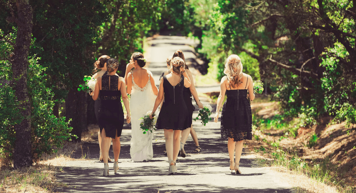 A group of bridesmaids walking in all black with the bride in all white
